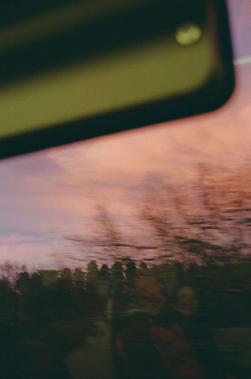 Blurred landscape view through a window with trees silhouetted against a pink and purple sky.