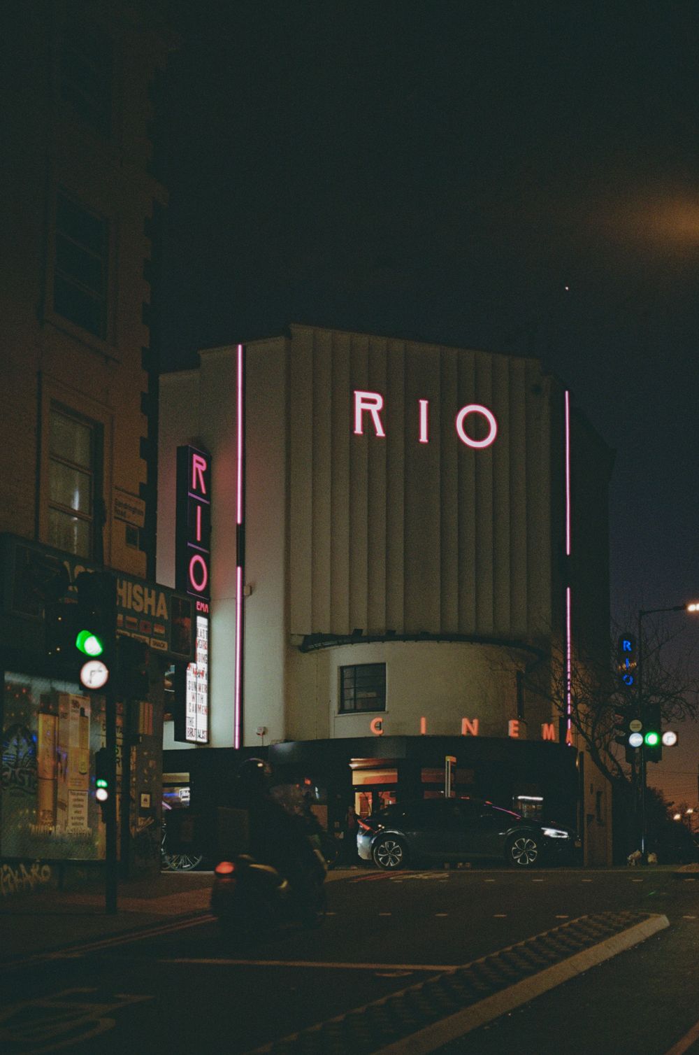 Art deco RIO cinema facade lit up at night with vintage neon signage.
