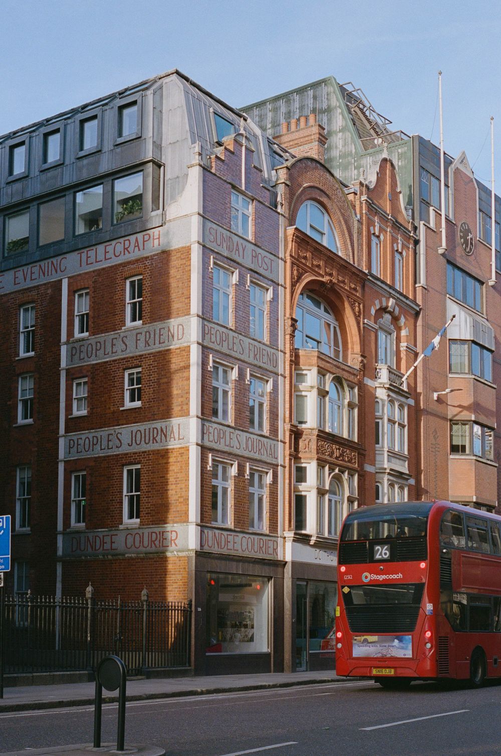 A historic brick building with 'The Telegraph' signage and a red London bus passing in front.