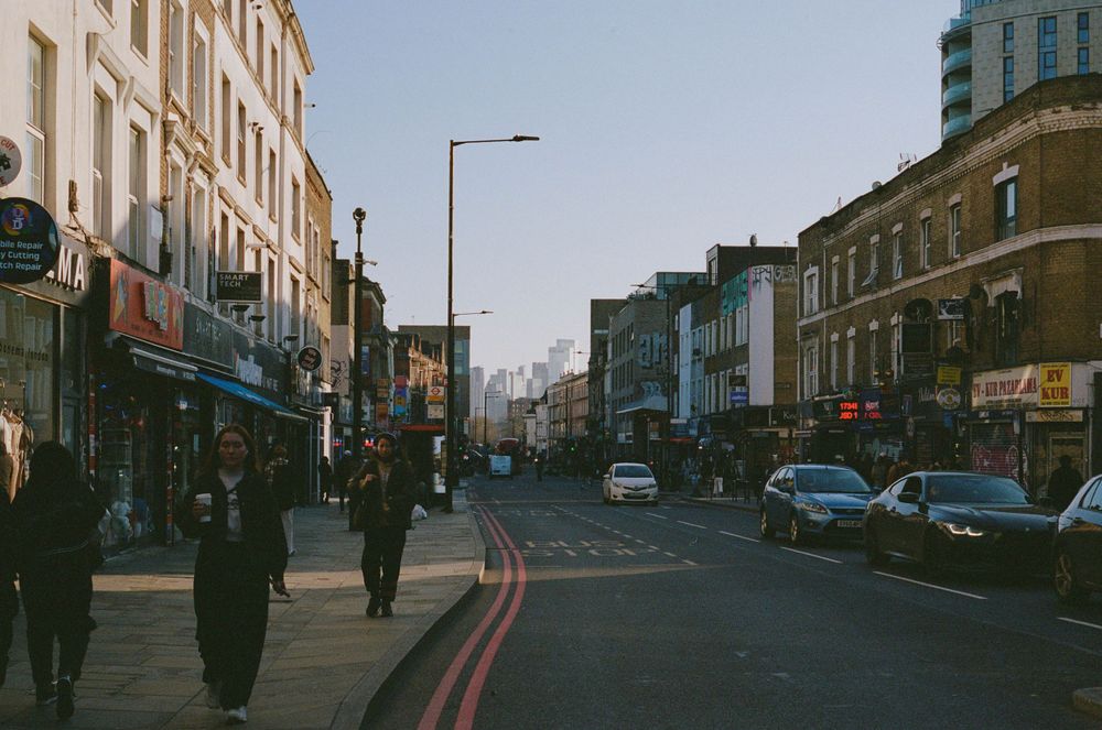 Bustling city street with shops and parked cars along storefronts in urban setting.