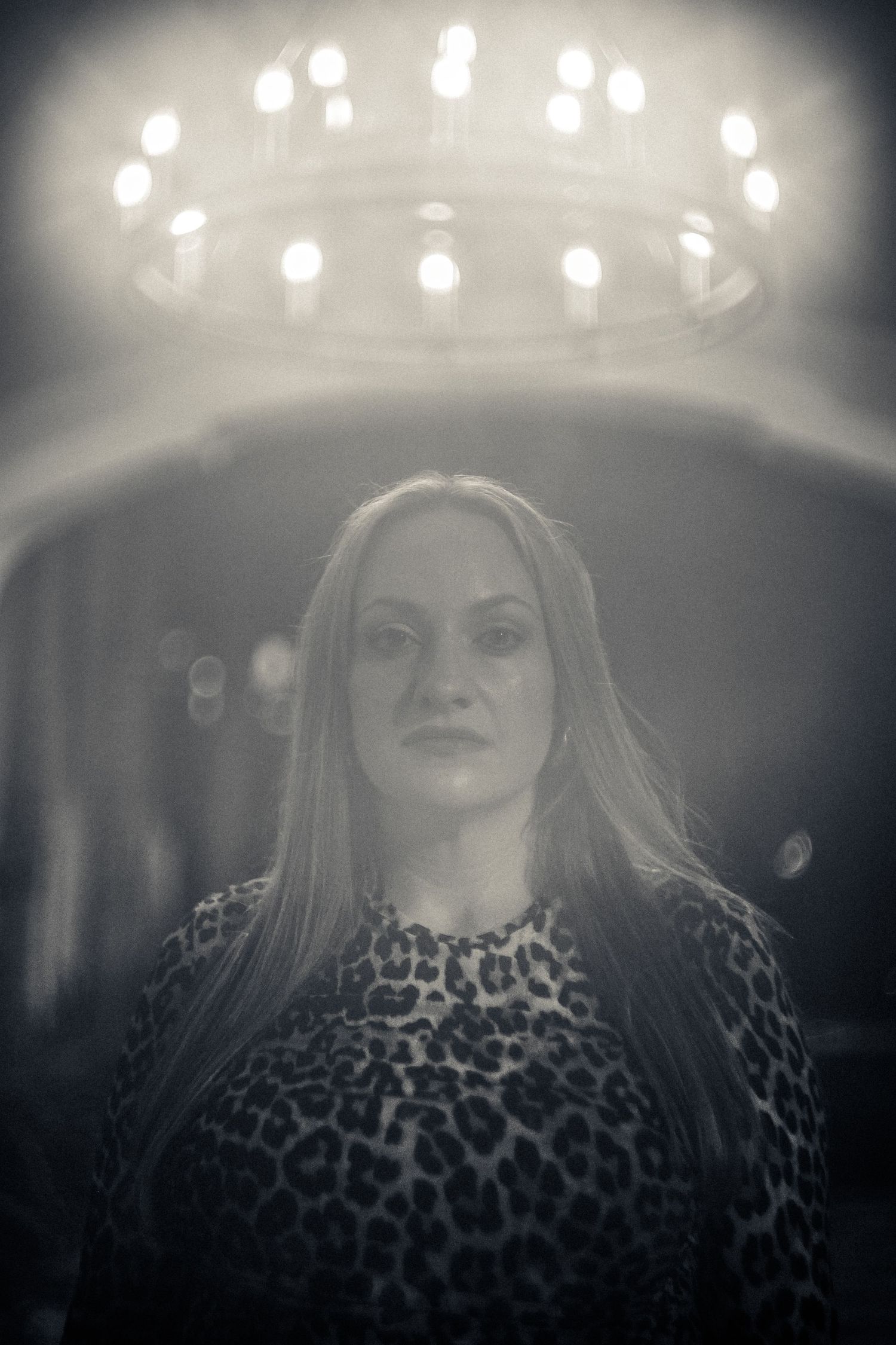 Black and white portrait with dramatic overhead chandelier lighting and a person wearing a leopard print top.