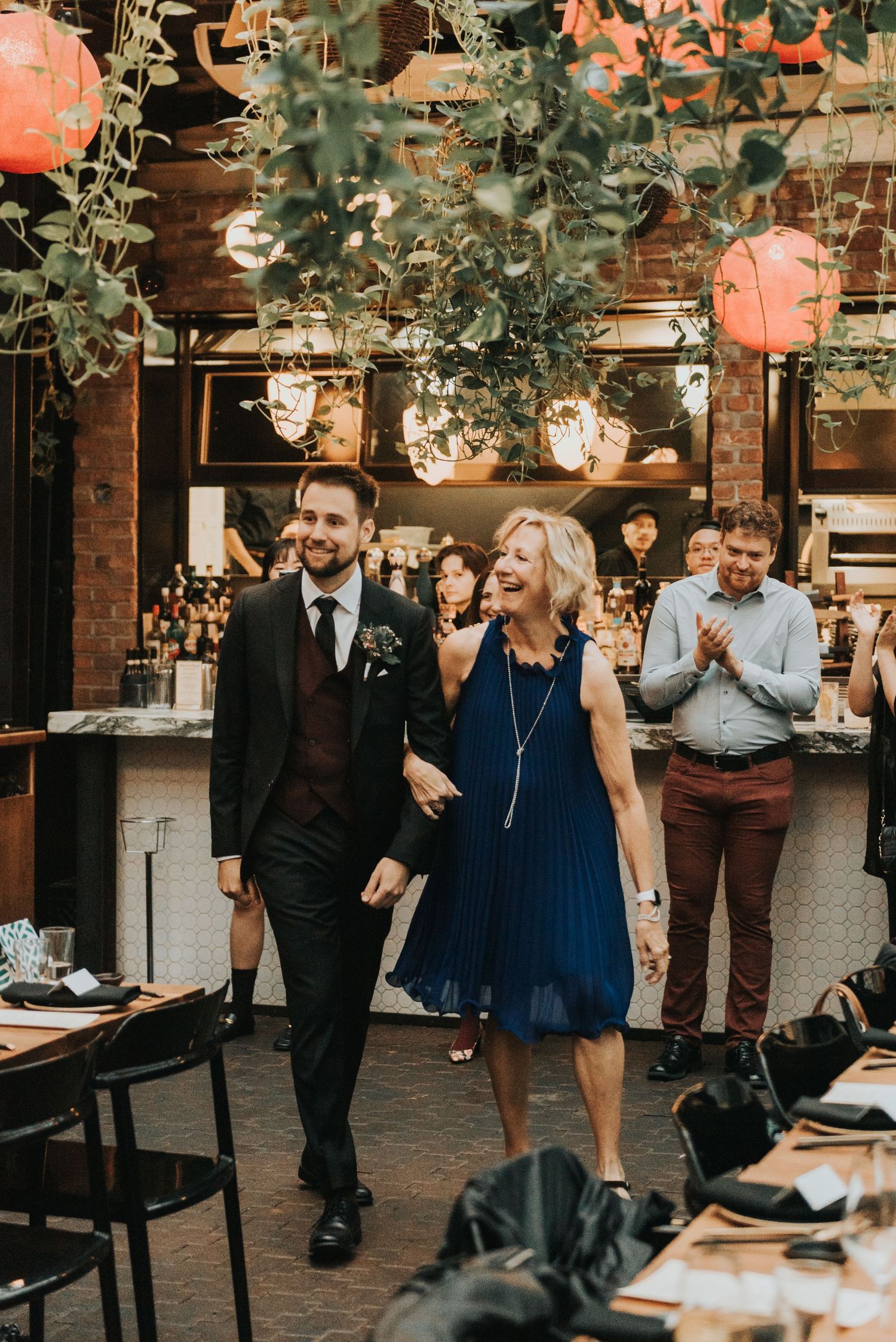 Outdoor wedding venue decorated with string lights and paper lanterns featuring guests laughing at a reception.