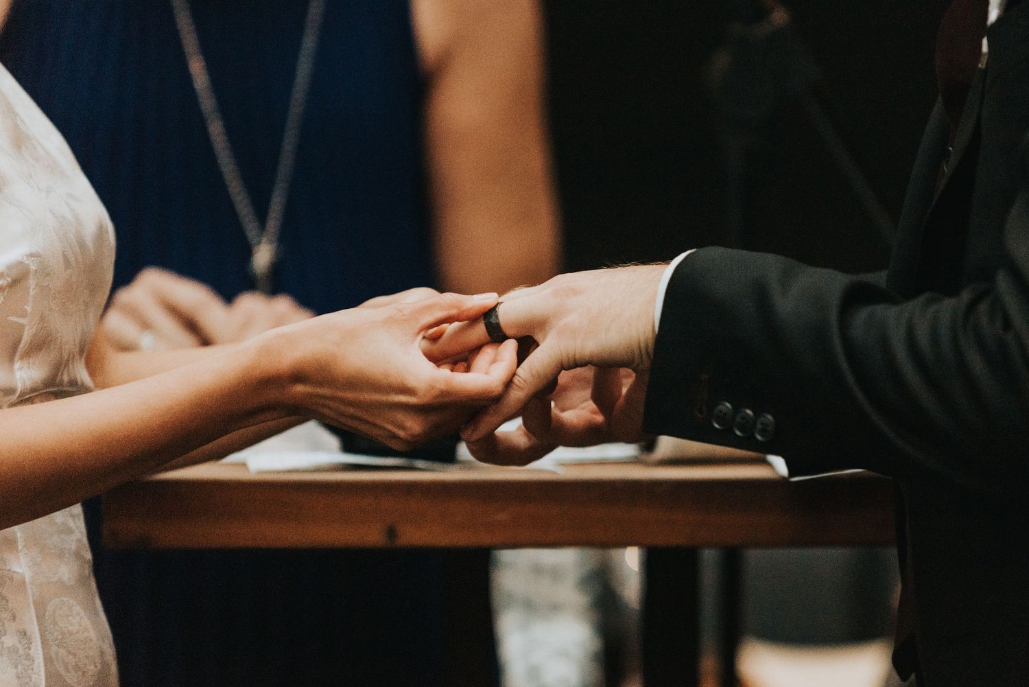Close-up shot of hands exchanging wedding rings during a ceremony at a wooden podium.