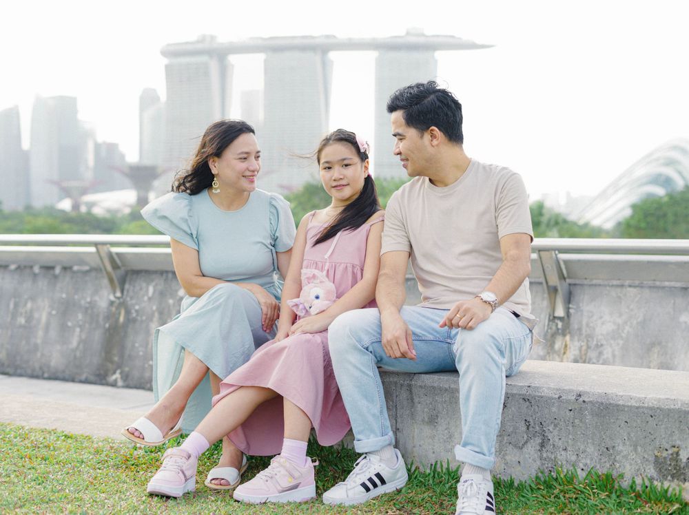 Three people sit together on a concrete wall with Singapore's iconic Marina Bay Sands hotel visible in the background.
