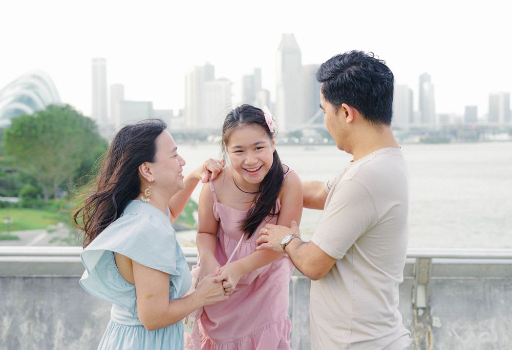 Three friends sharing a joyful moment together while laughing against a cityscape backdrop at the riverfront.