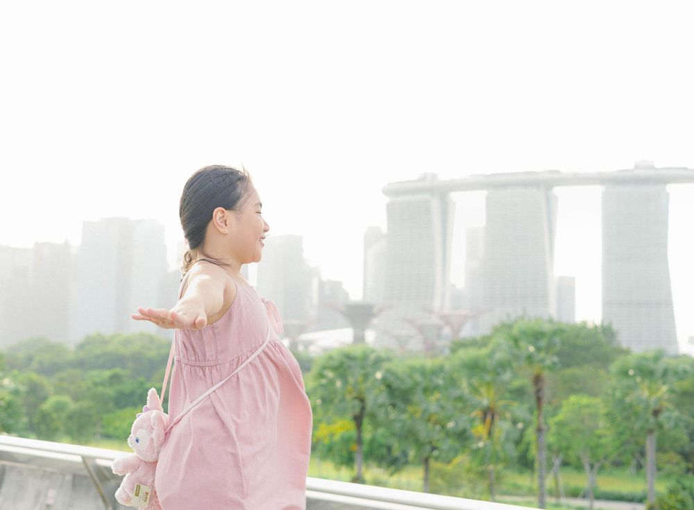 A person in pink dress stretches on a rooftop with Singapore's Marina Bay Sands hotel visible in the misty background.