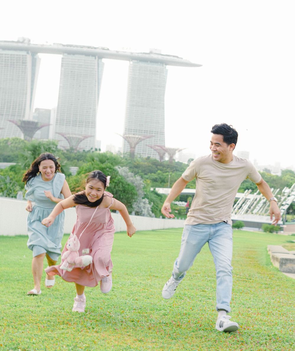 Family playing and running together on a grassy lawn with Marina Bay Sands hotel visible in the background in Singapore.