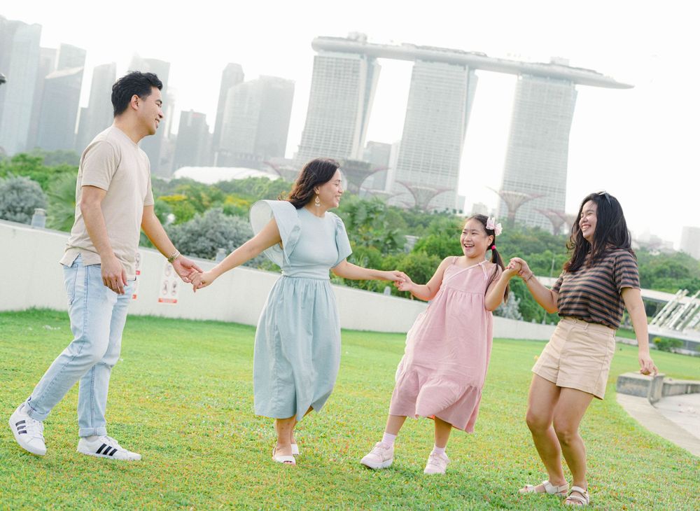 Happy family enjoying outdoor fun at Gardens by the Bay with Marina Bay Sands hotel in Singapore skyline background.