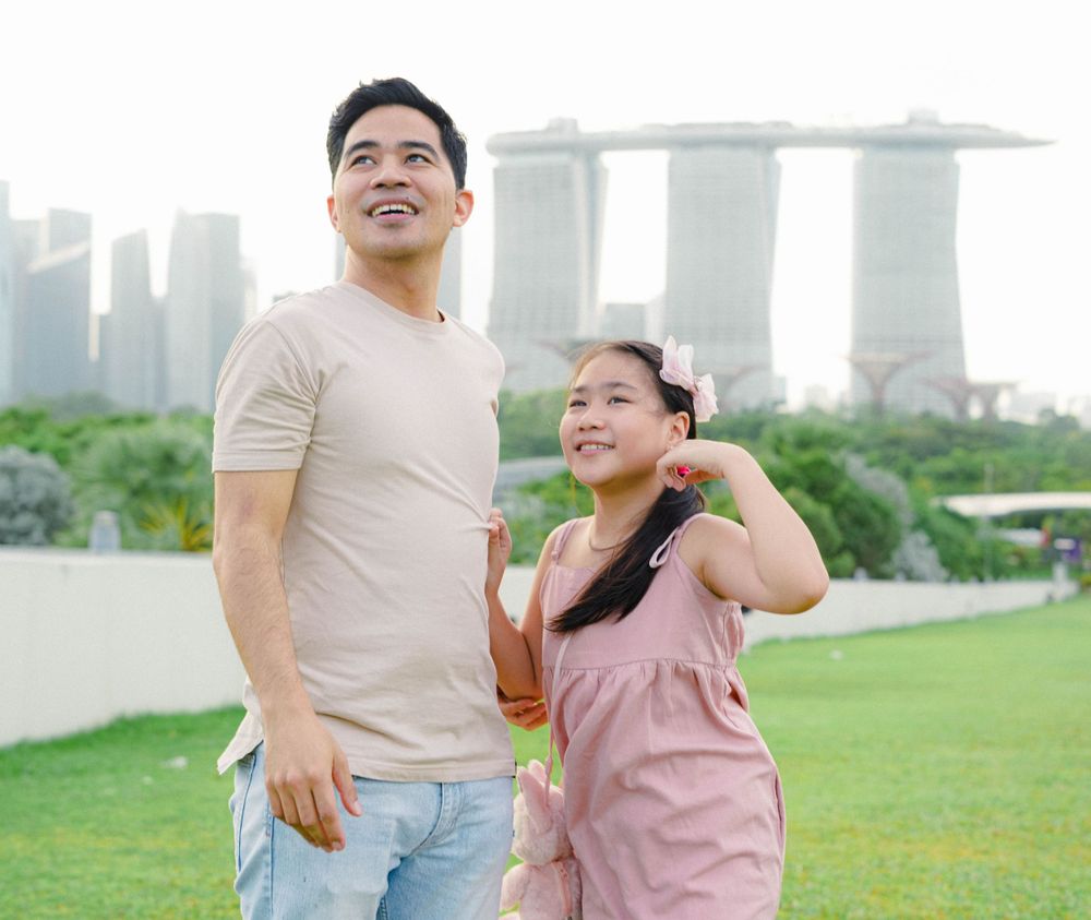 A happy couple enjoying a walk in a park with Marina Bay Sands and the Singapore skyline visible in the background.
