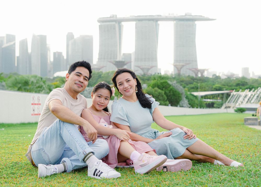 A family relaxes together on a grassy lawn with Singapore's Marina Bay Sands hotel and skyline visible in the background.
