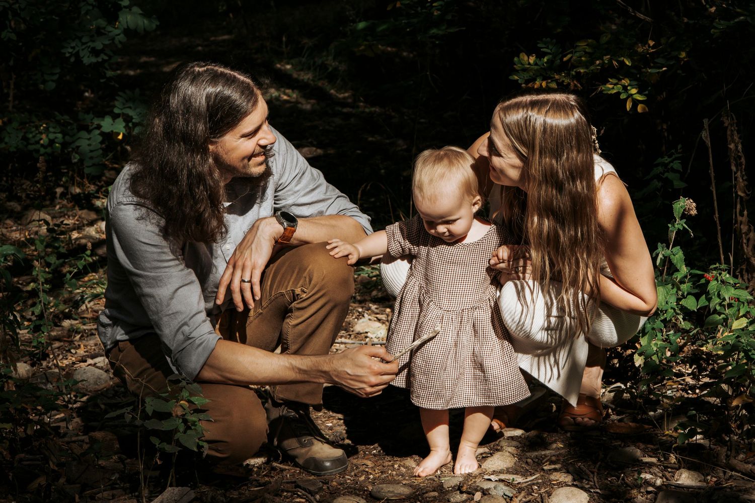 A family shares a tender outdoor moment together in a sunlit wooded area during a photo session.