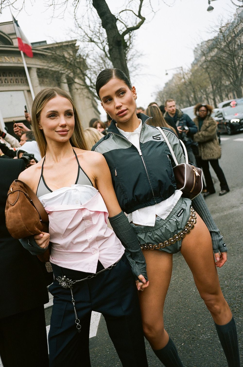 Models pose together on a city street during fashion week wearing stylish athleisure outfits and designer bags.