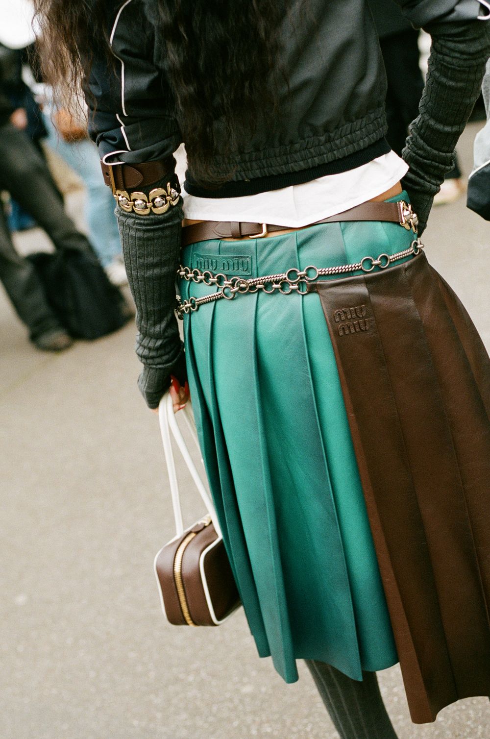 Fashionable green and brown pleated skirt with chain detail and black top shown from the side.