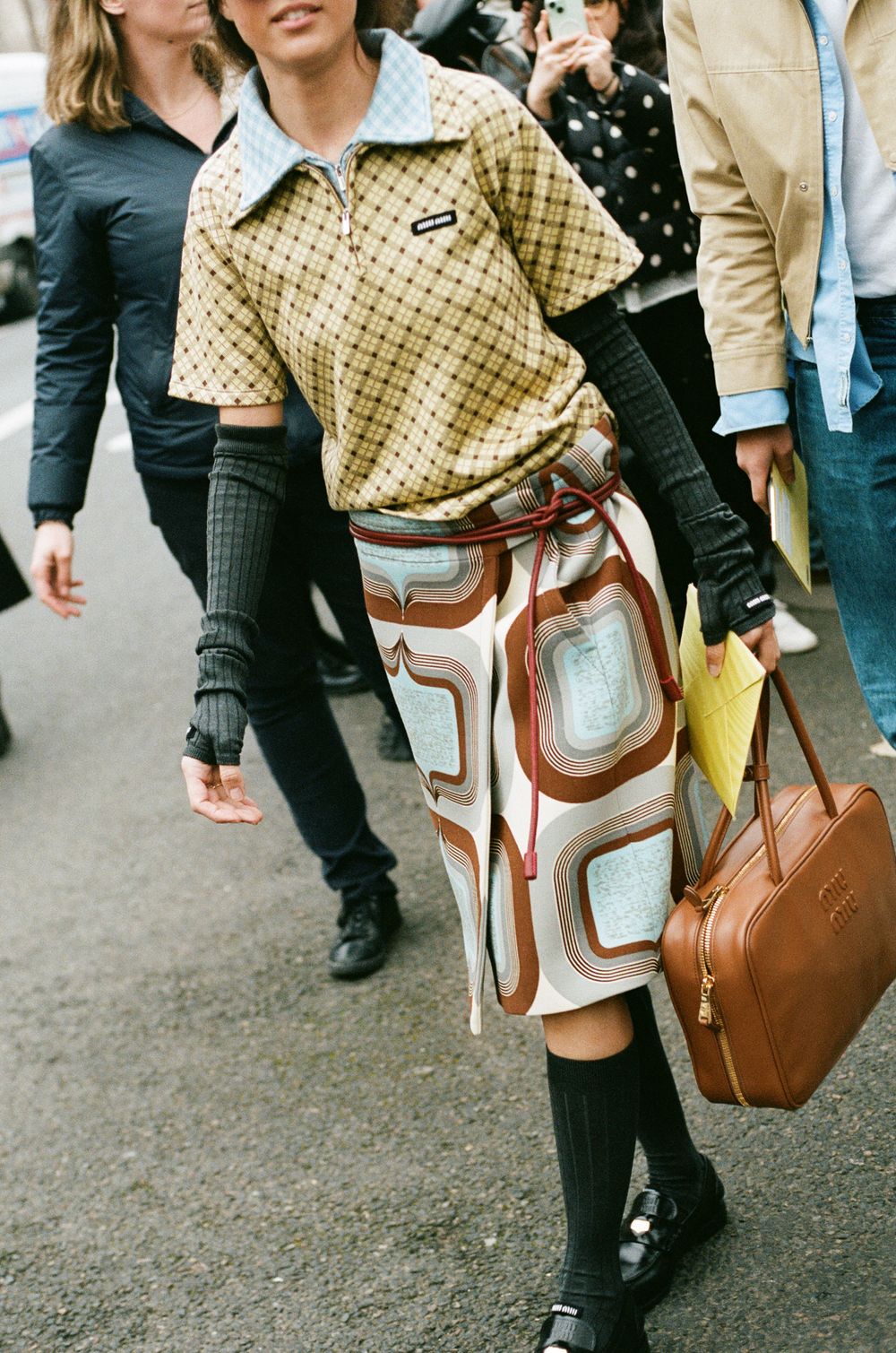 Retro 70s style outfit with patterned skirt, knee socks and yellow Nike polo shirt spotted at fashion event.