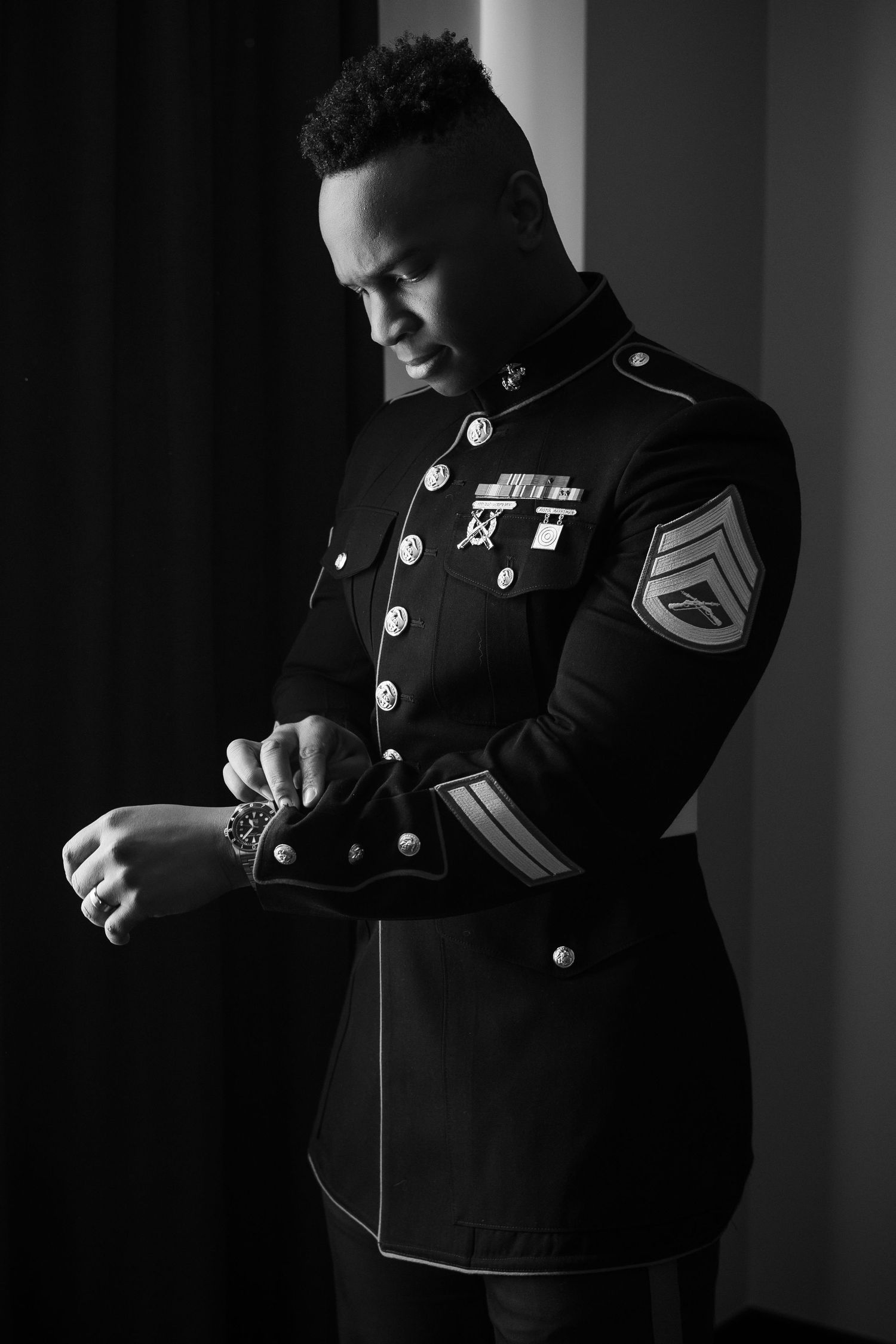 Dramatic black and white portrait of a Marine in dress uniform adjusting his sleeve.