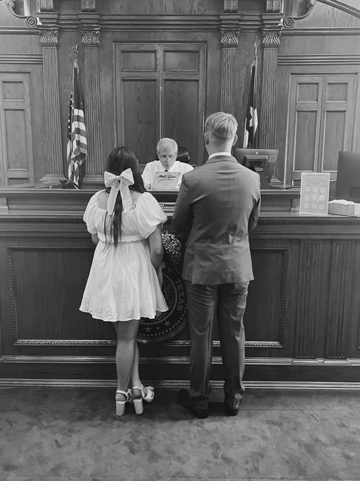 A couple stands before a judge in a courtroom during what appears to be a wedding ceremony.