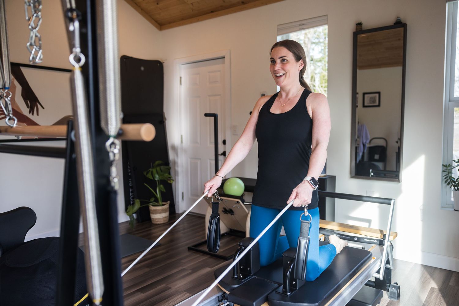 Someone exercises on a Pilates reformer machine during a workout session at a home studio.