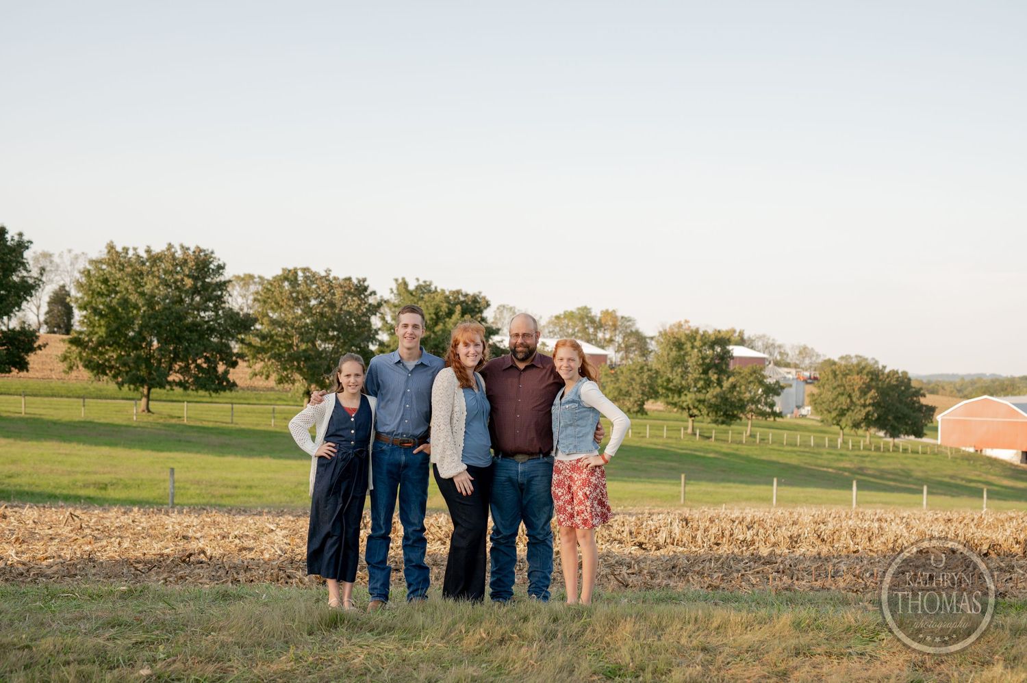 Family of five posing for outdoor photo with green rolling hills in background.