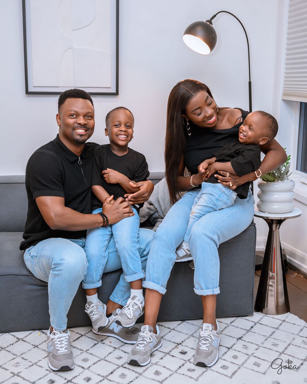 A family wearing matching light blue jeans and posing together on a gray couch in their living room.