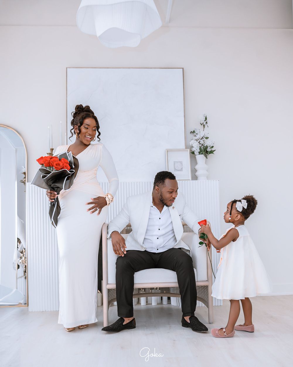 A family poses playfully in a white room with arched details, wearing elegant white outfits for a formal portrait session.