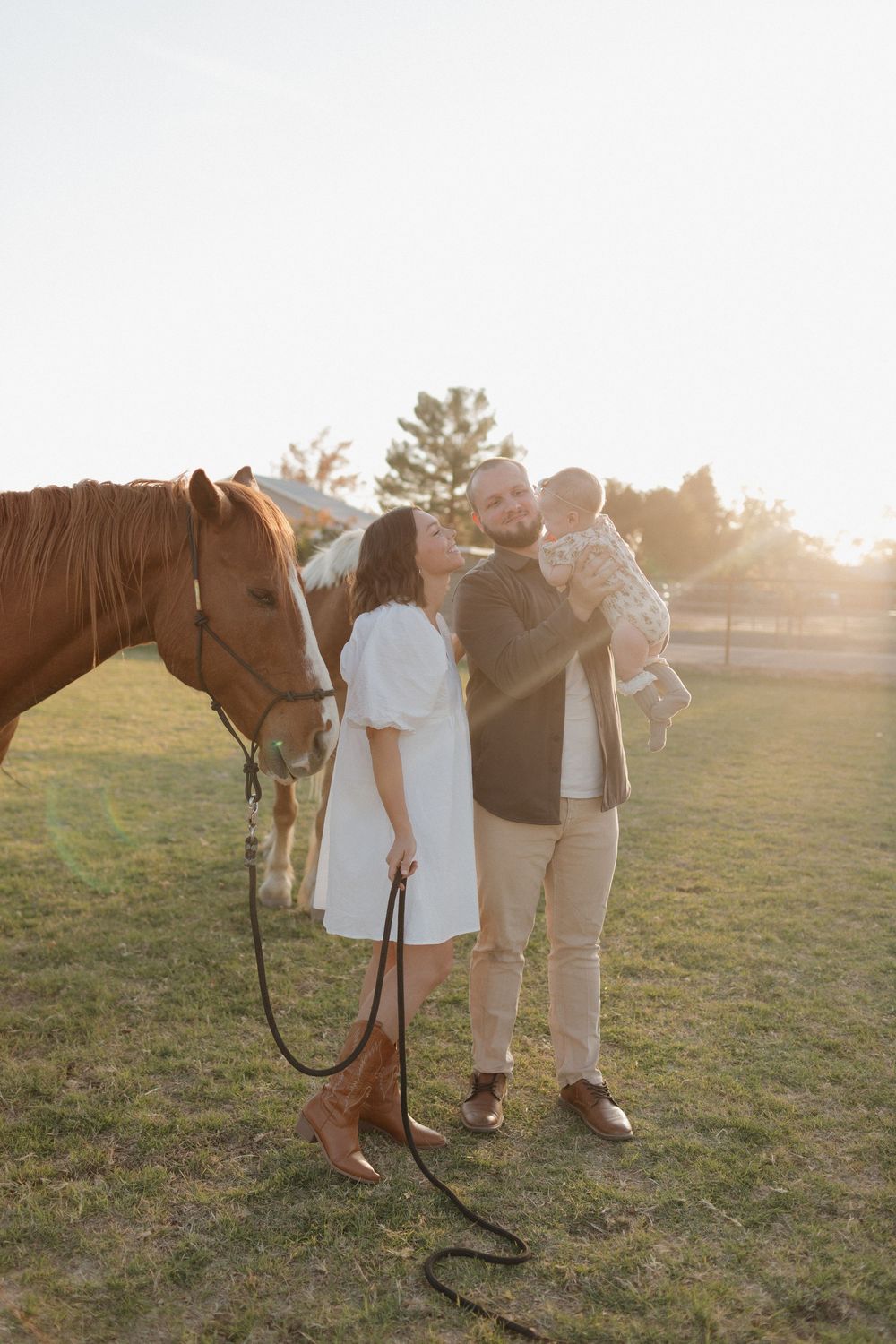 Family stands with a chestnut horse in a grassy field during golden hour sunset.
