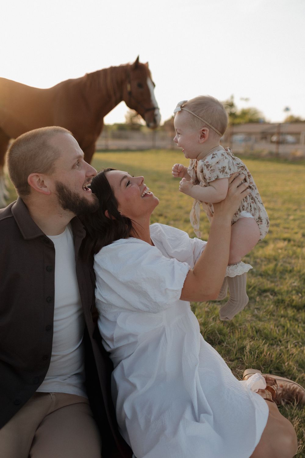 Joyful family moment with horse watching in background during sunset.