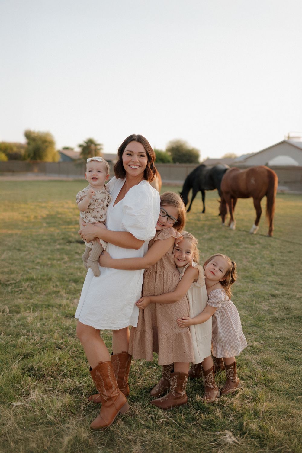 Family wearing coordinated outfits and boots poses in field with horses.