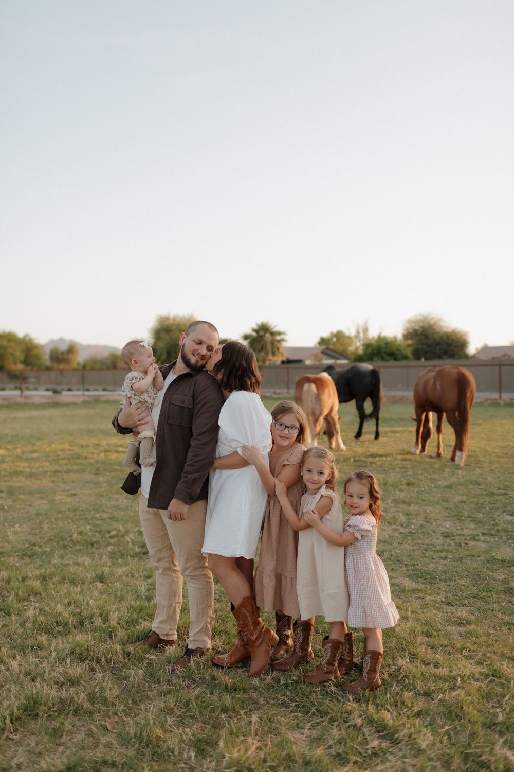 Intimate family portrait in a field during golden hour with horses in the background.