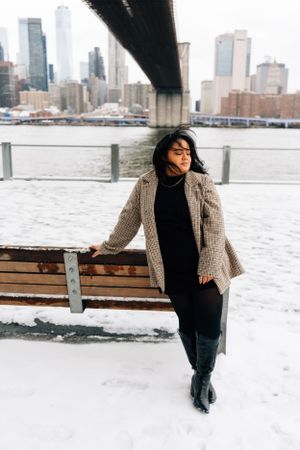 Snow covered winterscape in New York City with figure in chunky knit cardigan and black boots against urban skyline.