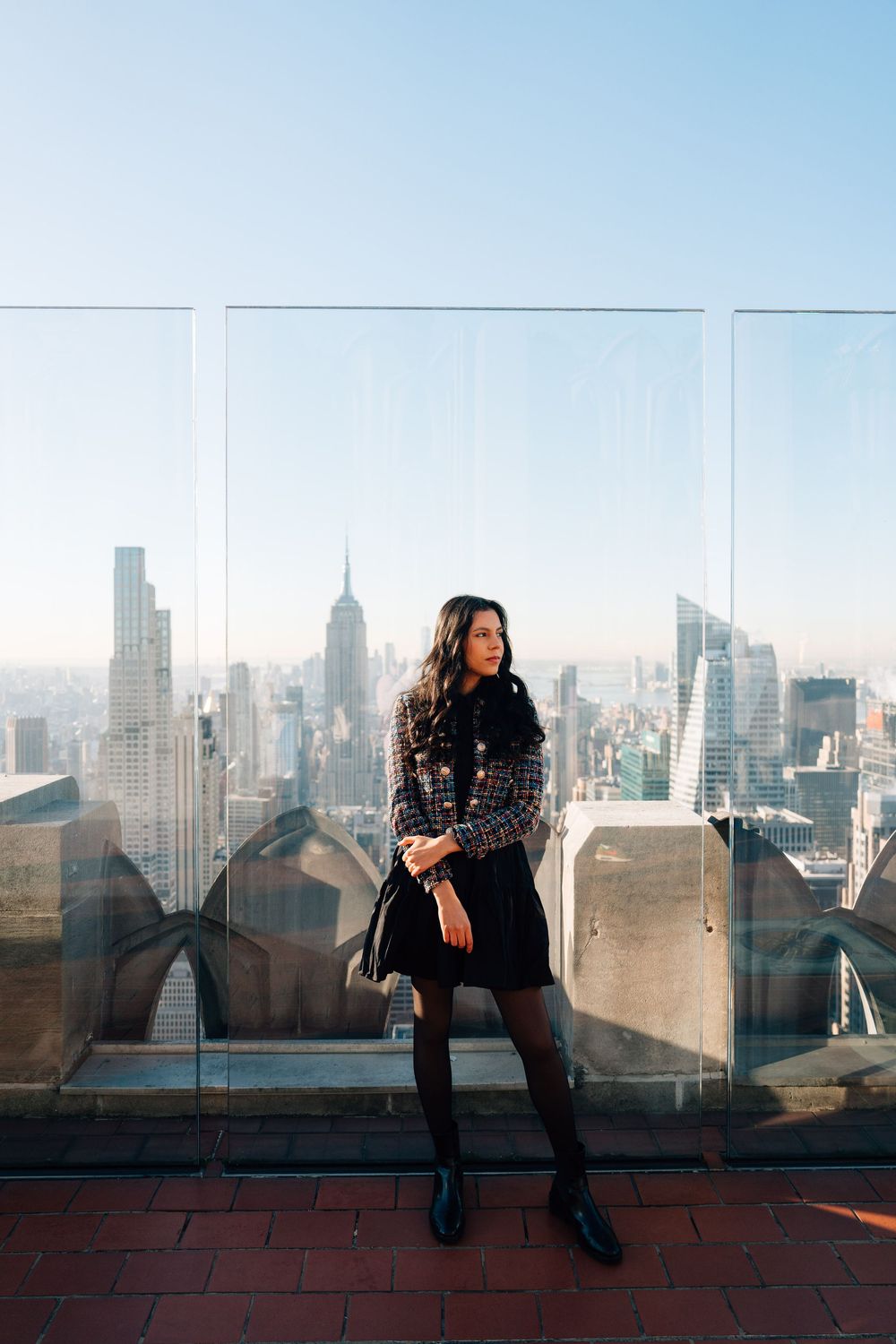 A silhouette sits on a rooftop ledge against the New York City skyline at sunset with multiple reflections.