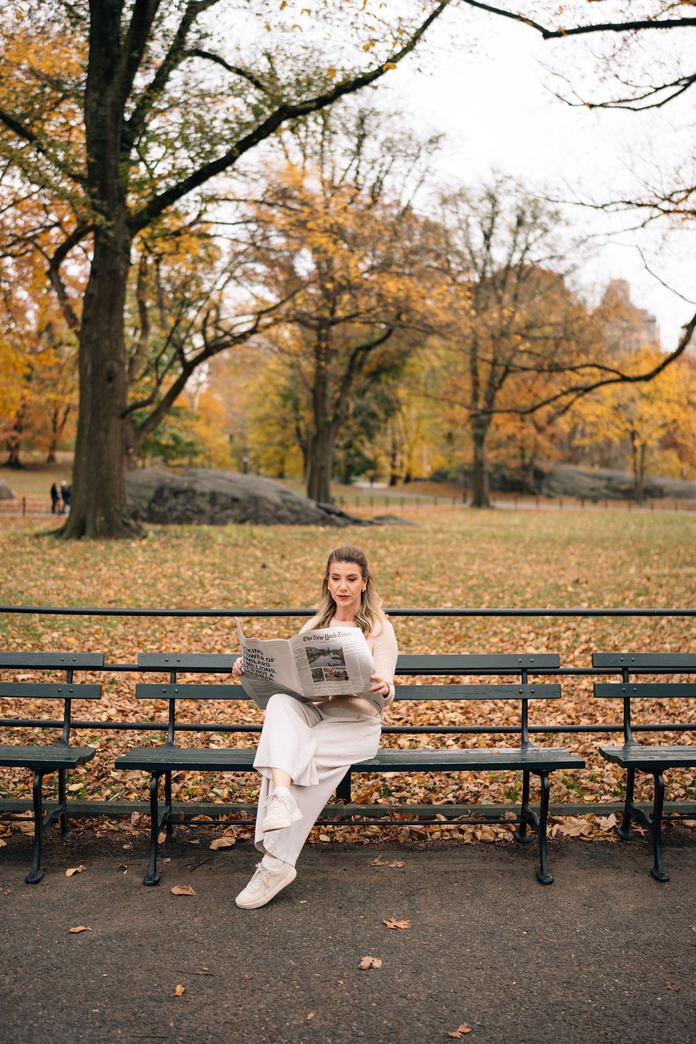 A person lounges on a park bench surrounded by autumn leaves in Central Park on a fall day.