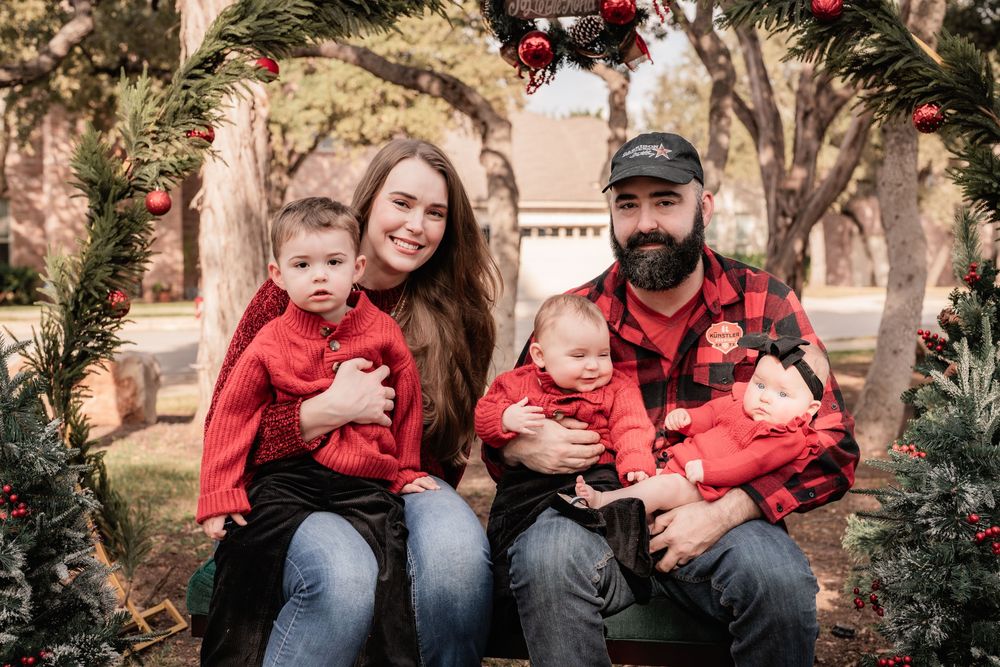Family wearing red and black buffalo plaid sits together on bench for outdoor holiday photo session.