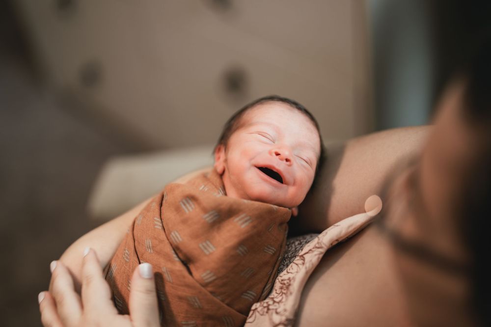 A close-up view of a newborn baby yawning while being cradled in gentle hands.