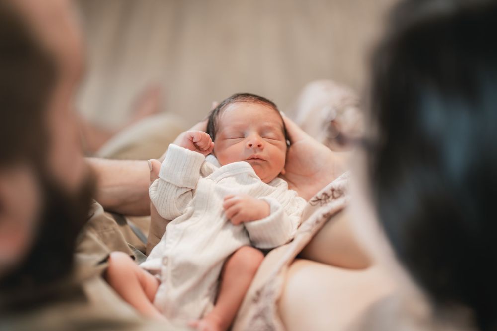 A sleeping newborn baby wearing white clothing rests peacefully on a soft surface.