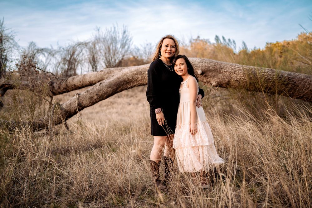 Two figures stand together in flowing dresses against rustic natural backdrop with fallen logs.