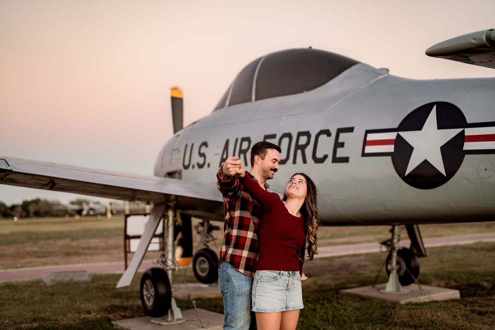 A couple poses in front of a vintage U.S. Air Force aircraft during sunset at an outdoor display.
