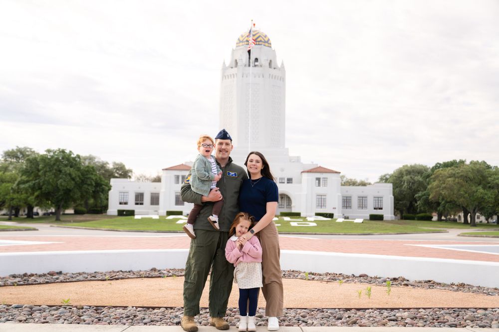 A family stands in front of a grand white building with a tower on a sunny day.