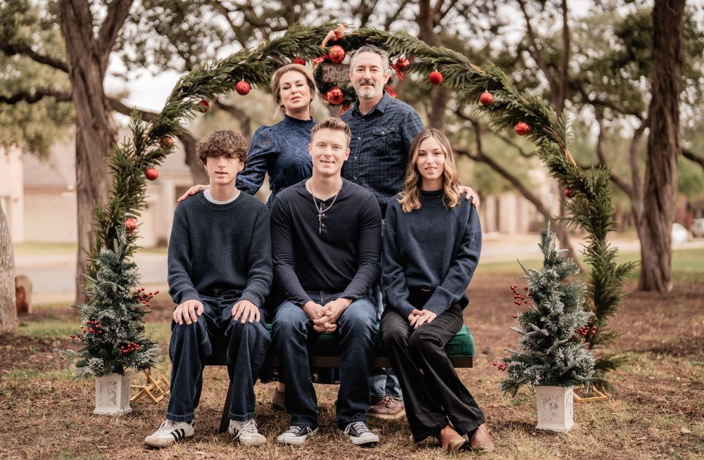 A group of people in dark clothing sit together outdoors for a casual family photo session.