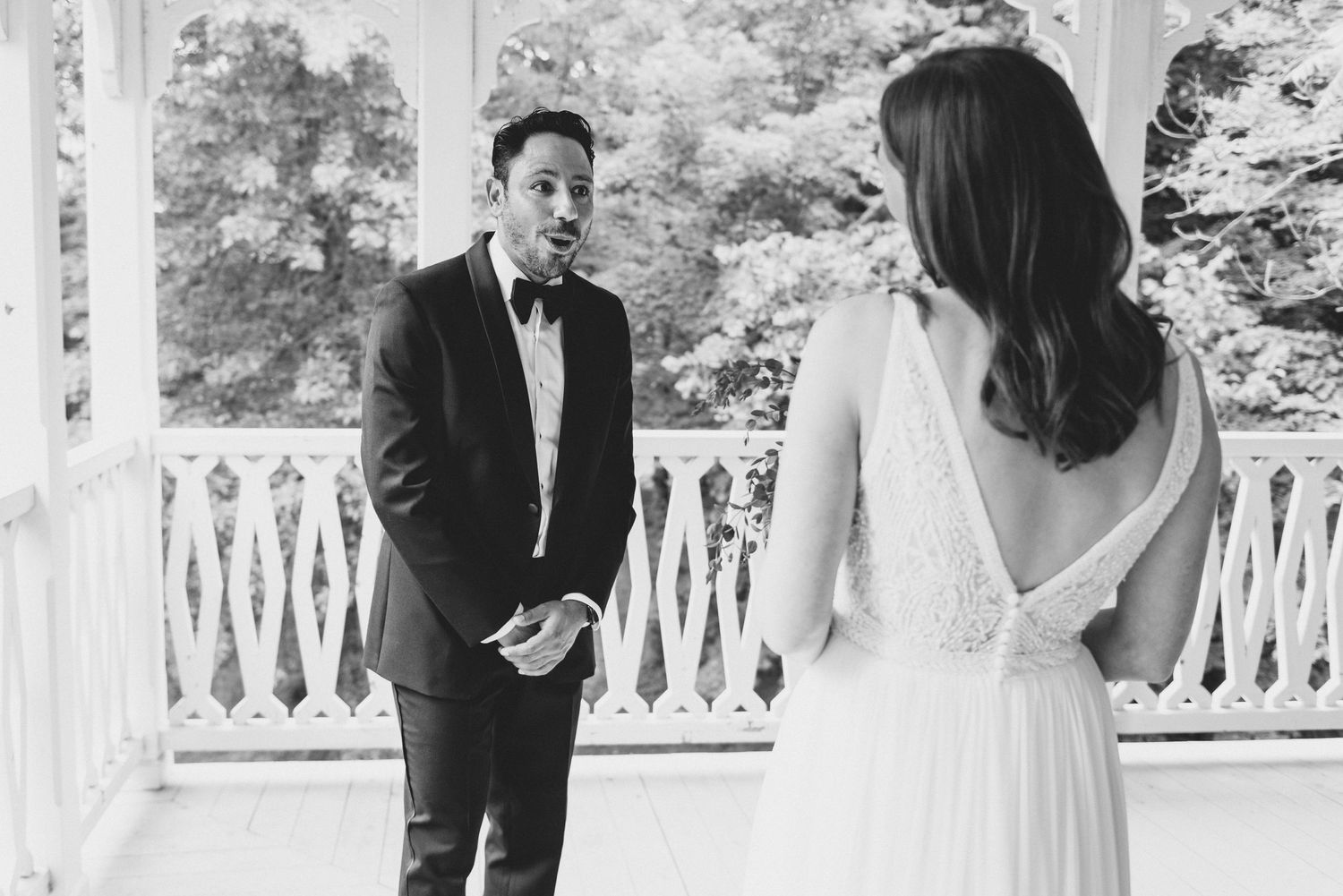 A black and white photo captures an emotional first look moment between newlyweds on a classic white porch.