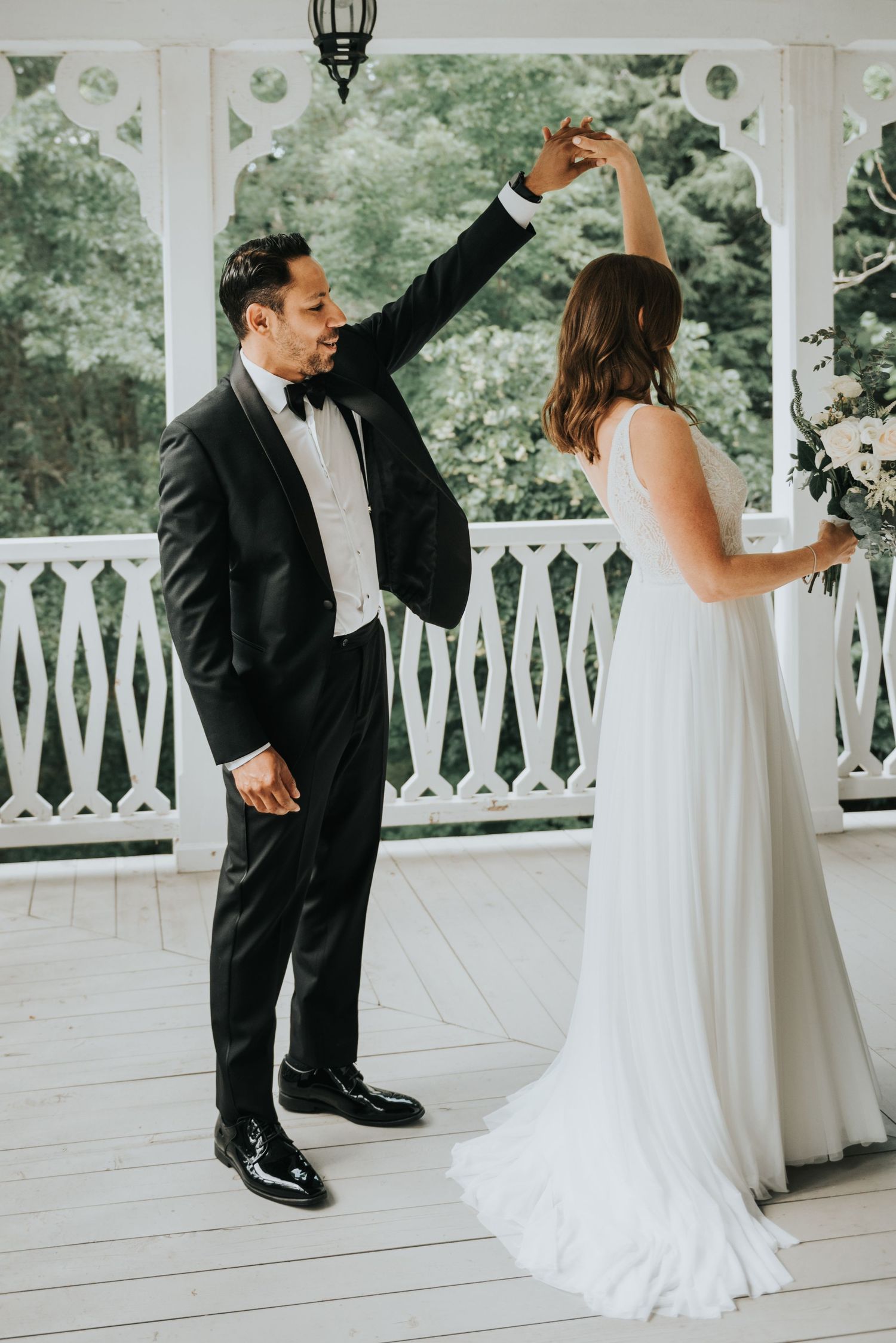 A couple shares their first dance on a white porch with ornate railings during their elegant outdoor wedding.