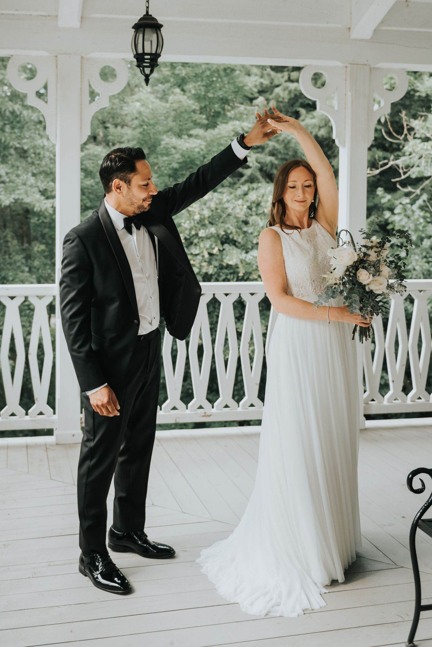 A couple share a dance on an elegant white porch with a lantern during their wedding celebration.