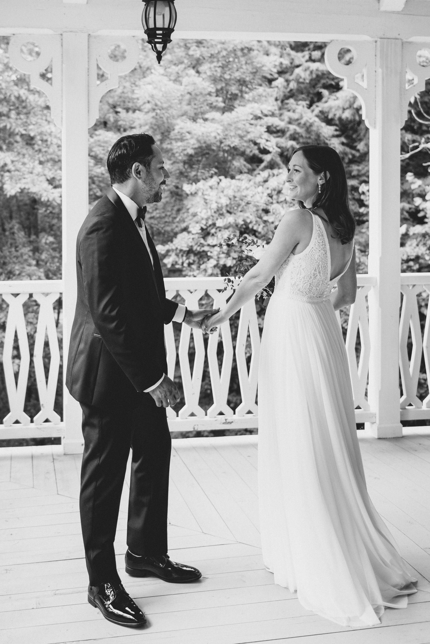 Black and white wedding photo of couple sharing a moment on an elegant white porch with railing and hanging lantern.
