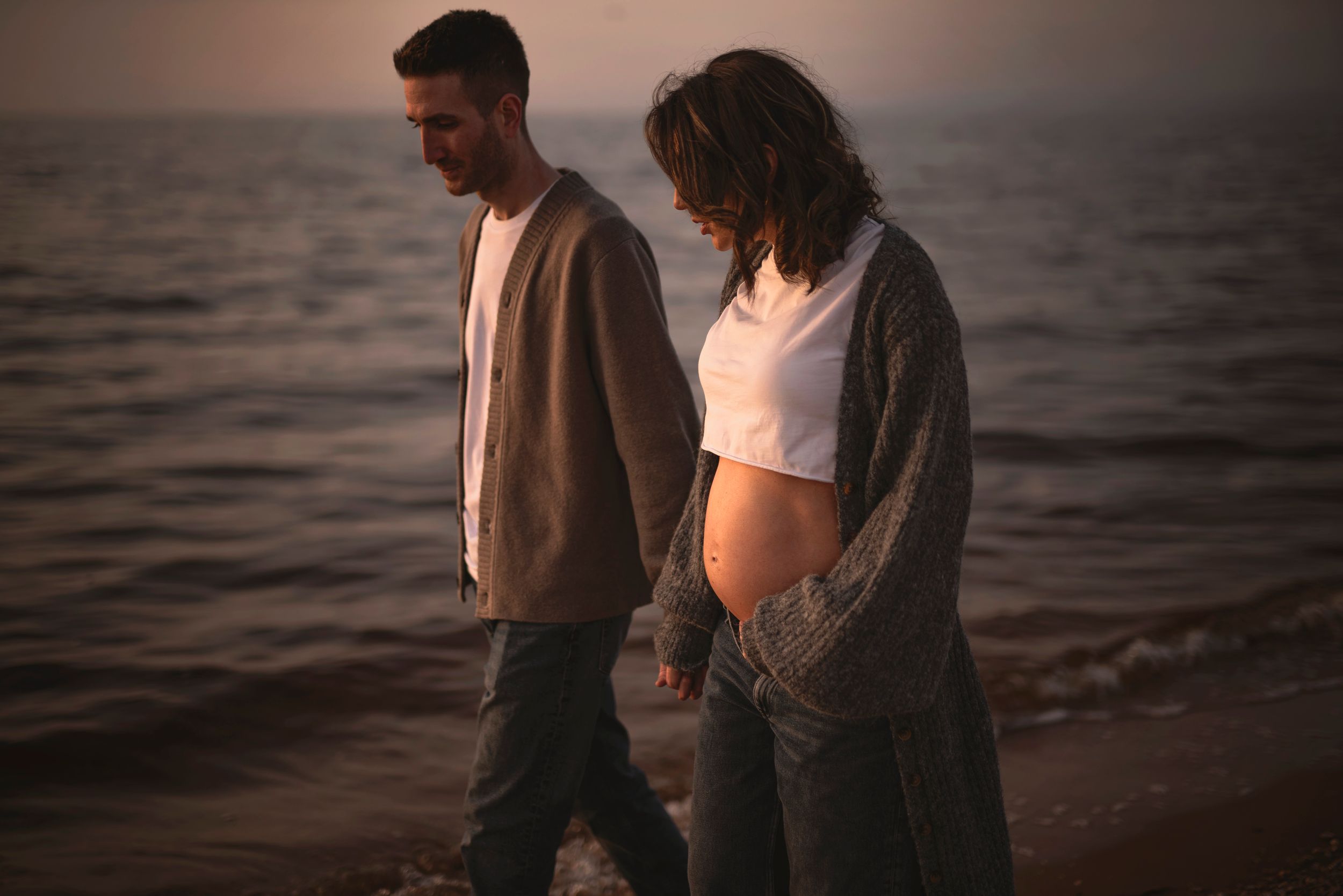 A couple walks along a misty beach at sunset wearing casual sweaters and enjoying the serene oceanfront atmosphere.