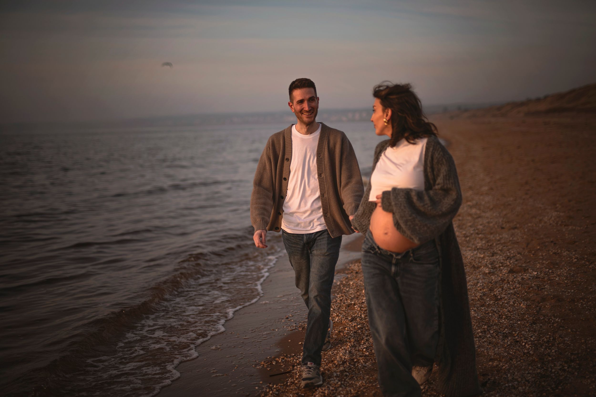 A couple walking together at sunset along a serene beach shoreline with waves lapping at their feet.