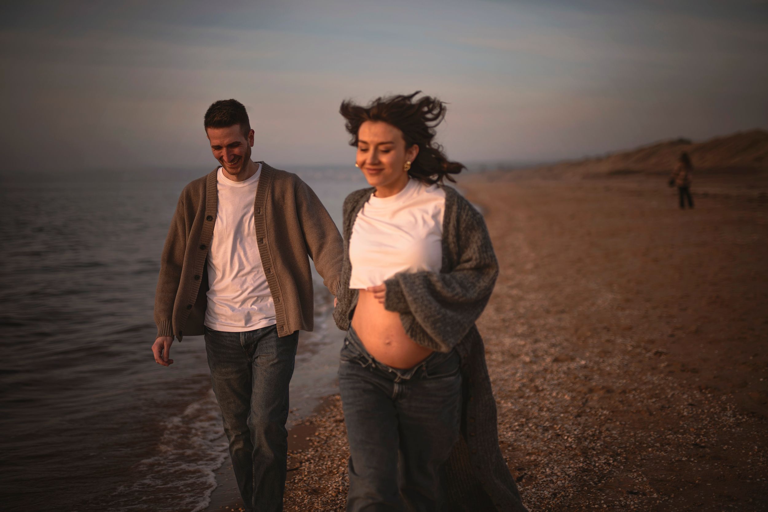 A couple strolls together on a sandy beach during golden hour wearing casual clothing.