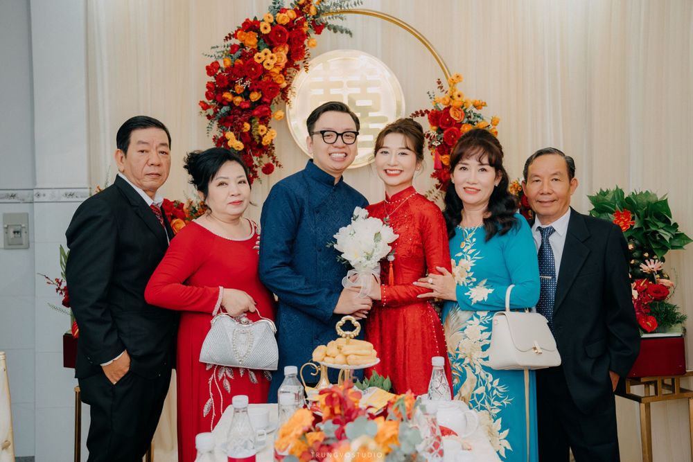 Vietnamese wedding family portrait with couple in ao dai and relatives before colorful floral backdrop.