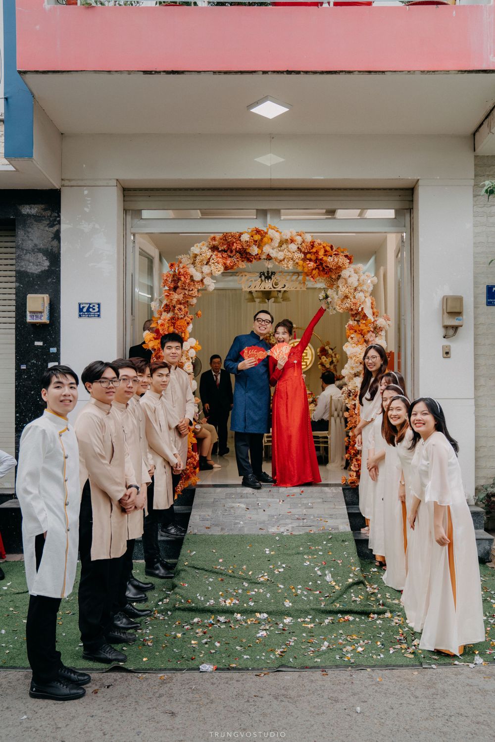Vietnamese wedding couple in ao dai exit flower arch greeted by bridesmaids and groomsmen lineup.