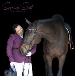 A rider in a purple jacket shares a tender moment with their brown horse against a black background.