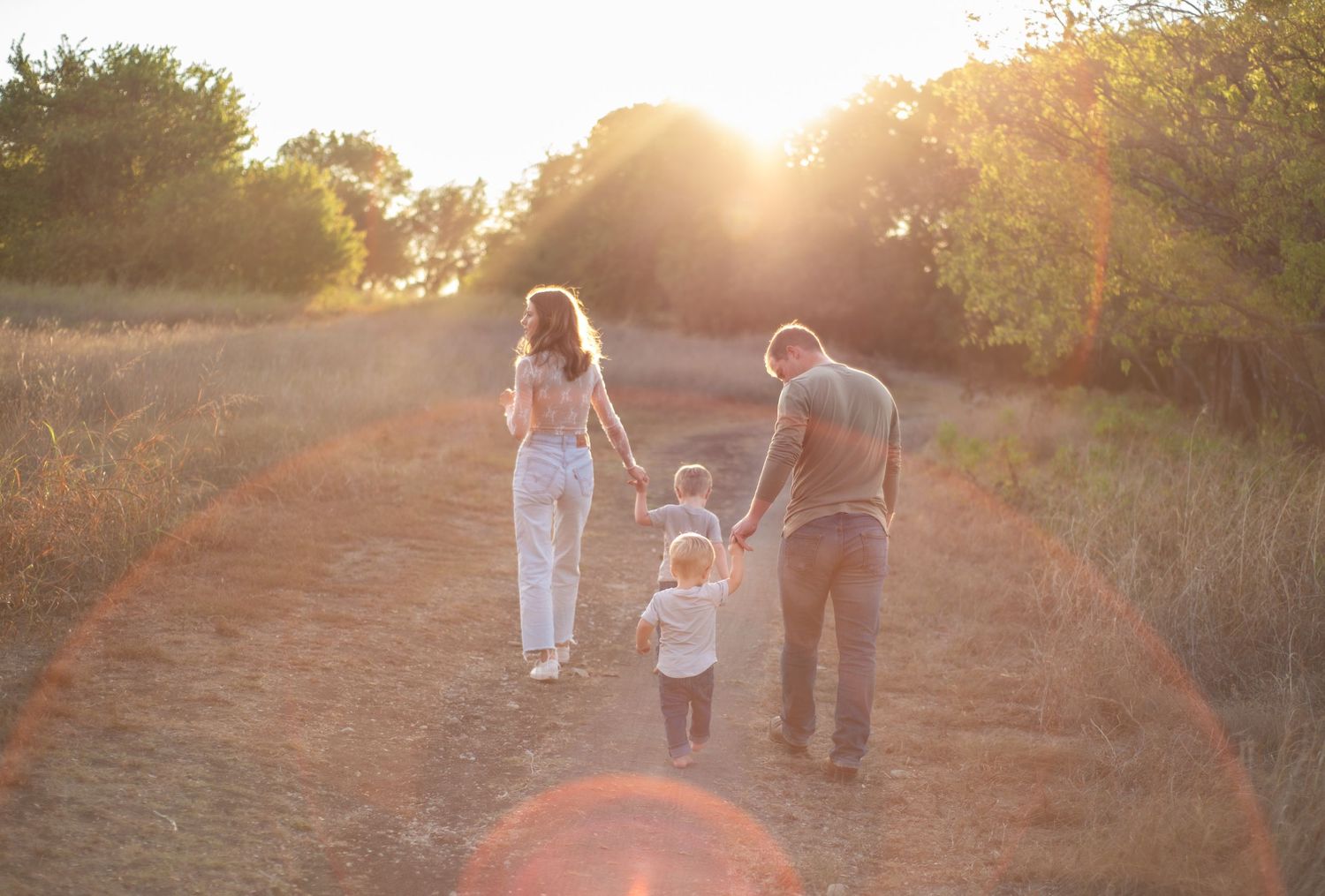 Three people walking on a dirt path during golden hour sunset with lens flare.