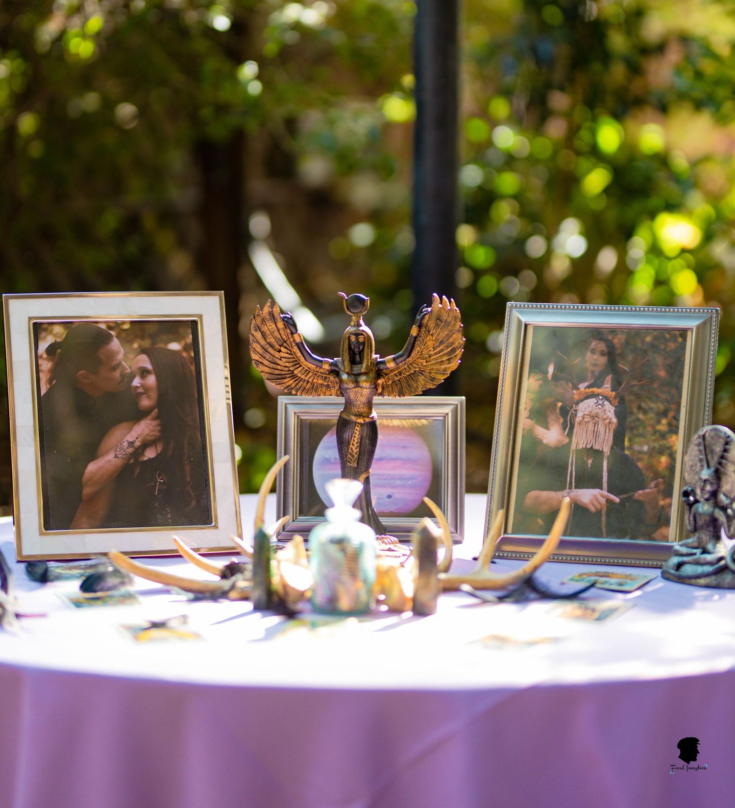Memorial table with framed photos and decorative Egyptian-style statue on purple tablecloth.